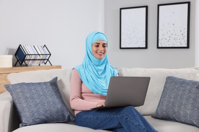 Muslim woman using laptop at couch in room