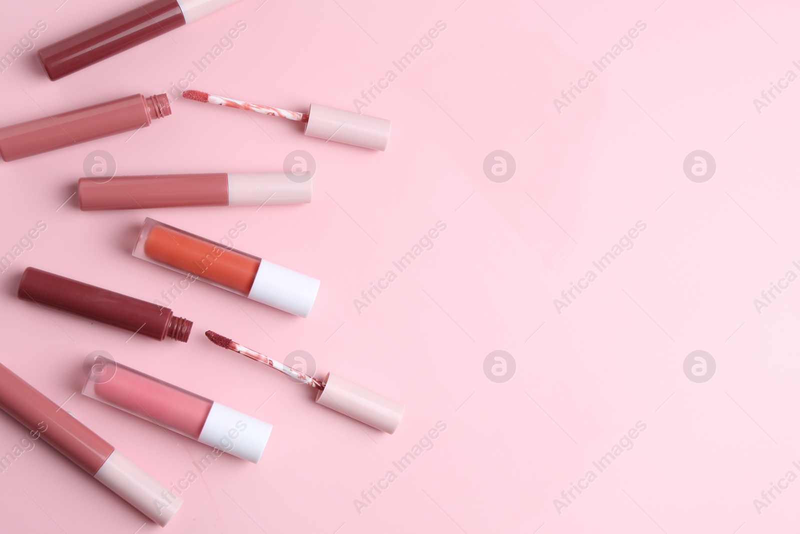 Photo of Different lip glosses and applicators on pink background, flat lay. Space for text