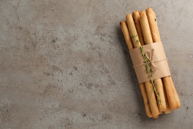 Delicious grissini sticks with thyme on grey table, top view. Space for text