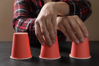 Photo of Woman playing thimblerig game with red cups at black table, closeup