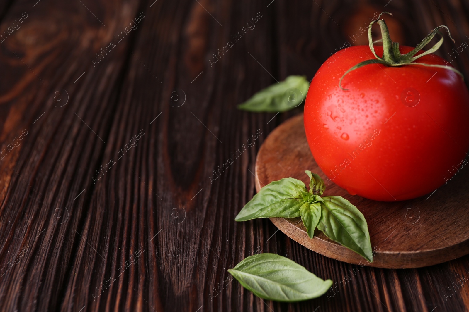 Photo of Fresh ripe tomato with water drops and basil leaves on wooden table, closeup. Space for text
