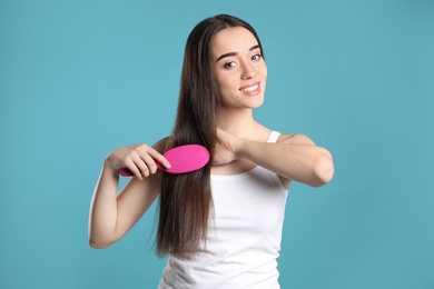 Photo of Beautiful smiling young woman with hair brush on color background