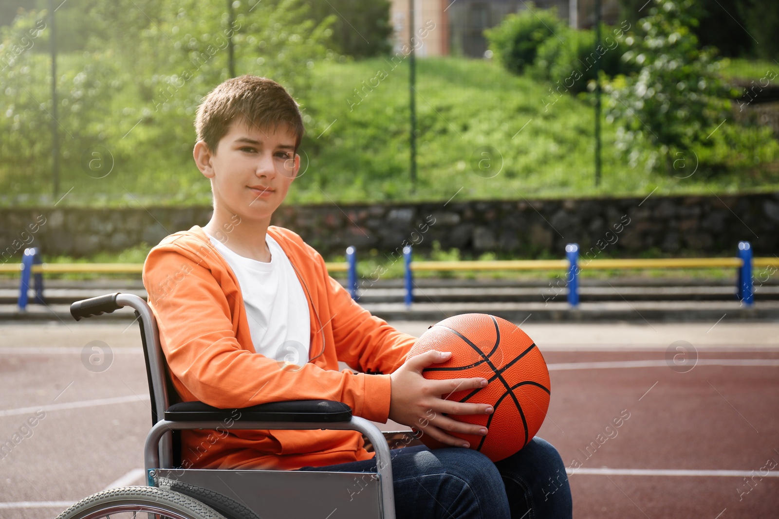 Photo of Disabled teenage boy in wheelchair with basketball ball at outdoor court