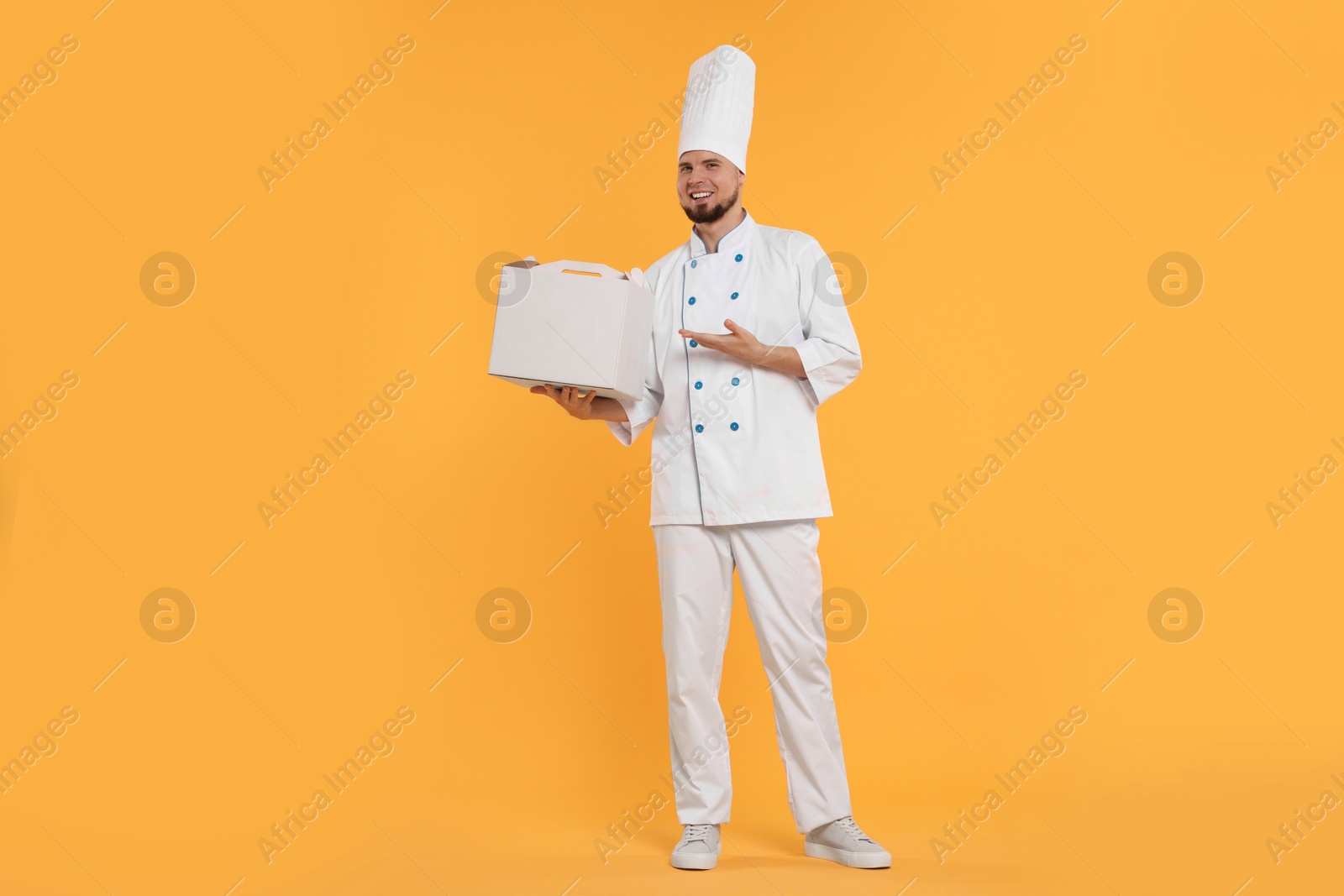 Photo of Happy professional confectioner in uniform holding cake box on yellow background