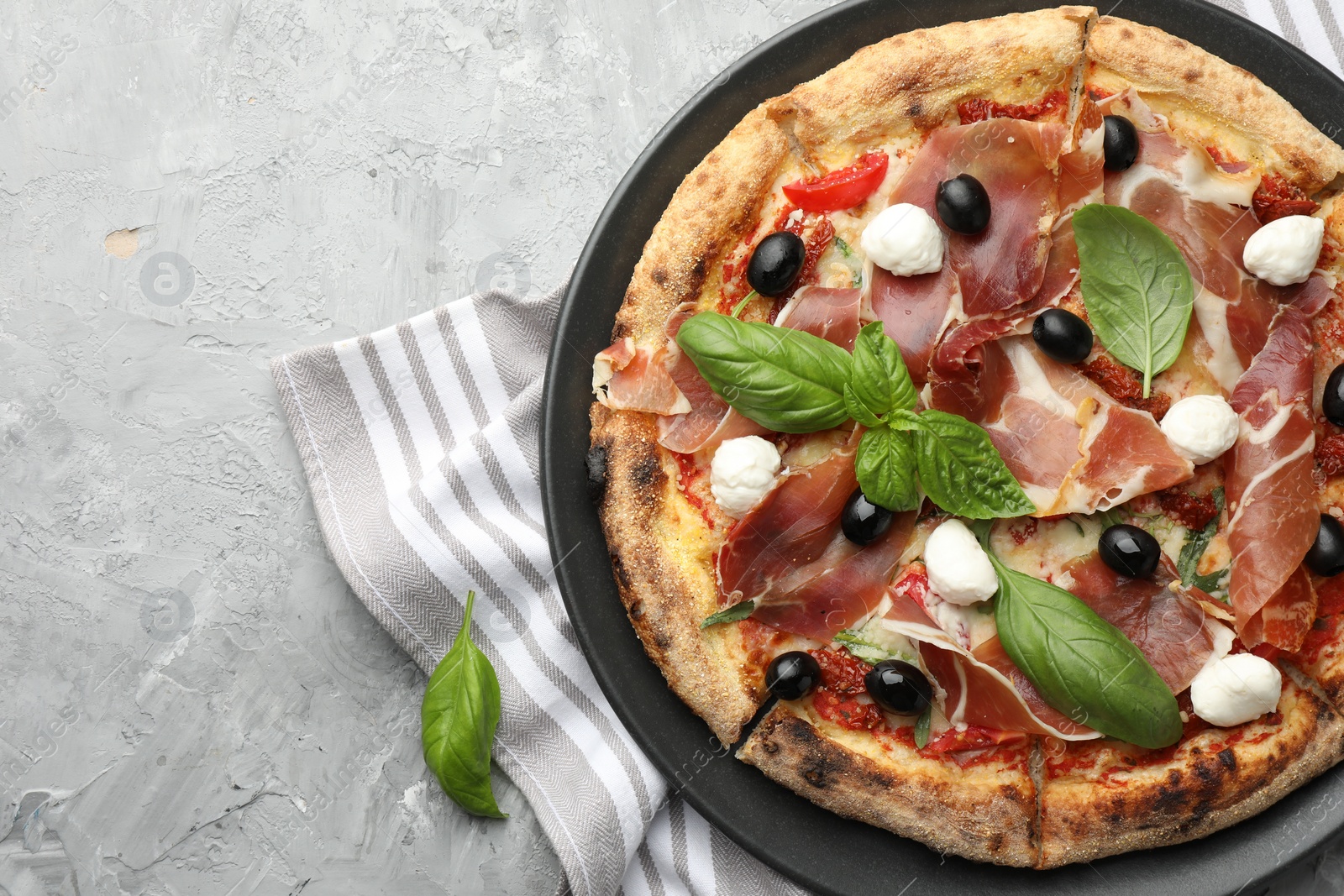 Photo of Tasty pizza with cured ham, olives, mozzarella cheese, sun-dried tomato and basil on gray textured table, top view. Space for text