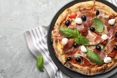 Tasty pizza with cured ham, olives, mozzarella cheese, sun-dried tomato and basil on gray textured table, top view. Space for text