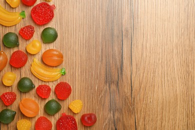 Delicious gummy fruit shaped candies on wooden table, flat lay. Space for text