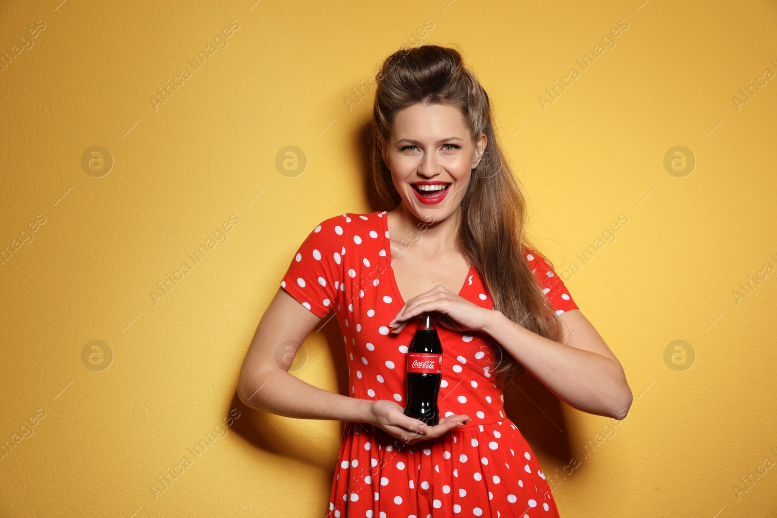 Photo of MYKOLAIV, UKRAINE - NOVEMBER 28, 2018: Young woman with bottle of Coca-Cola on color background