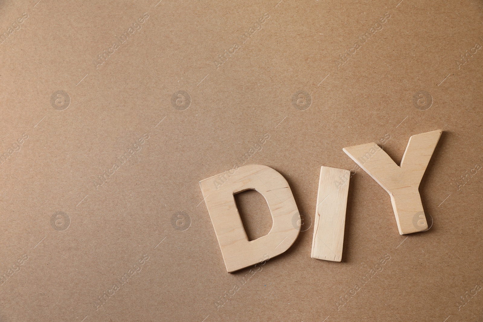 Photo of Abbreviation DIY made of wooden letters on light brown background, flat lay. Space for text