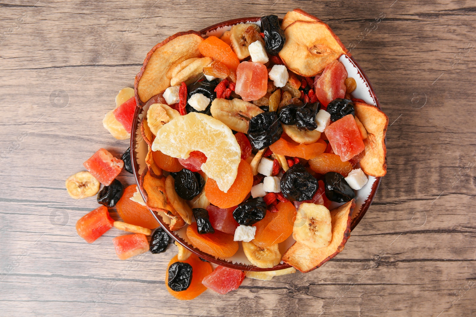 Photo of Bowl and different tasty dried fruits on wooden table, flat lay