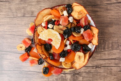 Bowl and different tasty dried fruits on wooden table, flat lay