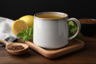 Photo of Cuparomatic buckwheat tea, spoon with granules, lemon and mint on wooden table, closeup