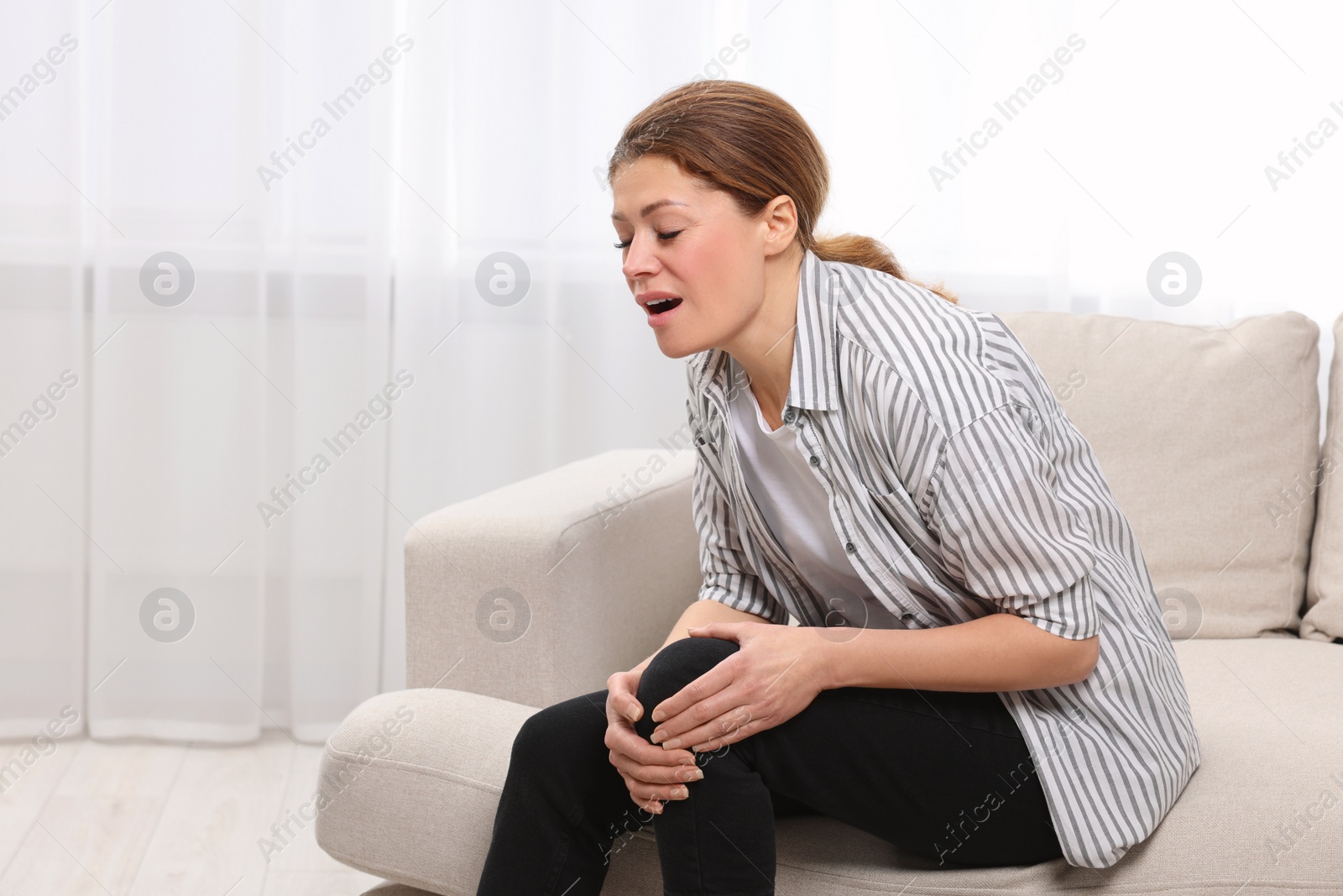 Photo of Woman suffering from knee pain on sofa indoors, space for text. Arthritis symptoms