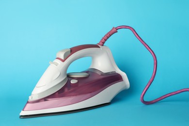 Photo of One modern iron on light blue background. Home appliance