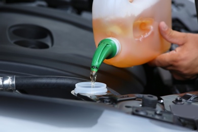 Man pouring liquid from plastic canister into car washer fluid reservoir, closeup