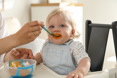 Mother feeding her cute little baby with healthy food at home