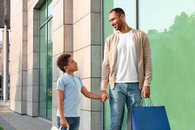 Family shopping. Happy father and son with colorful bags near mall outdoors