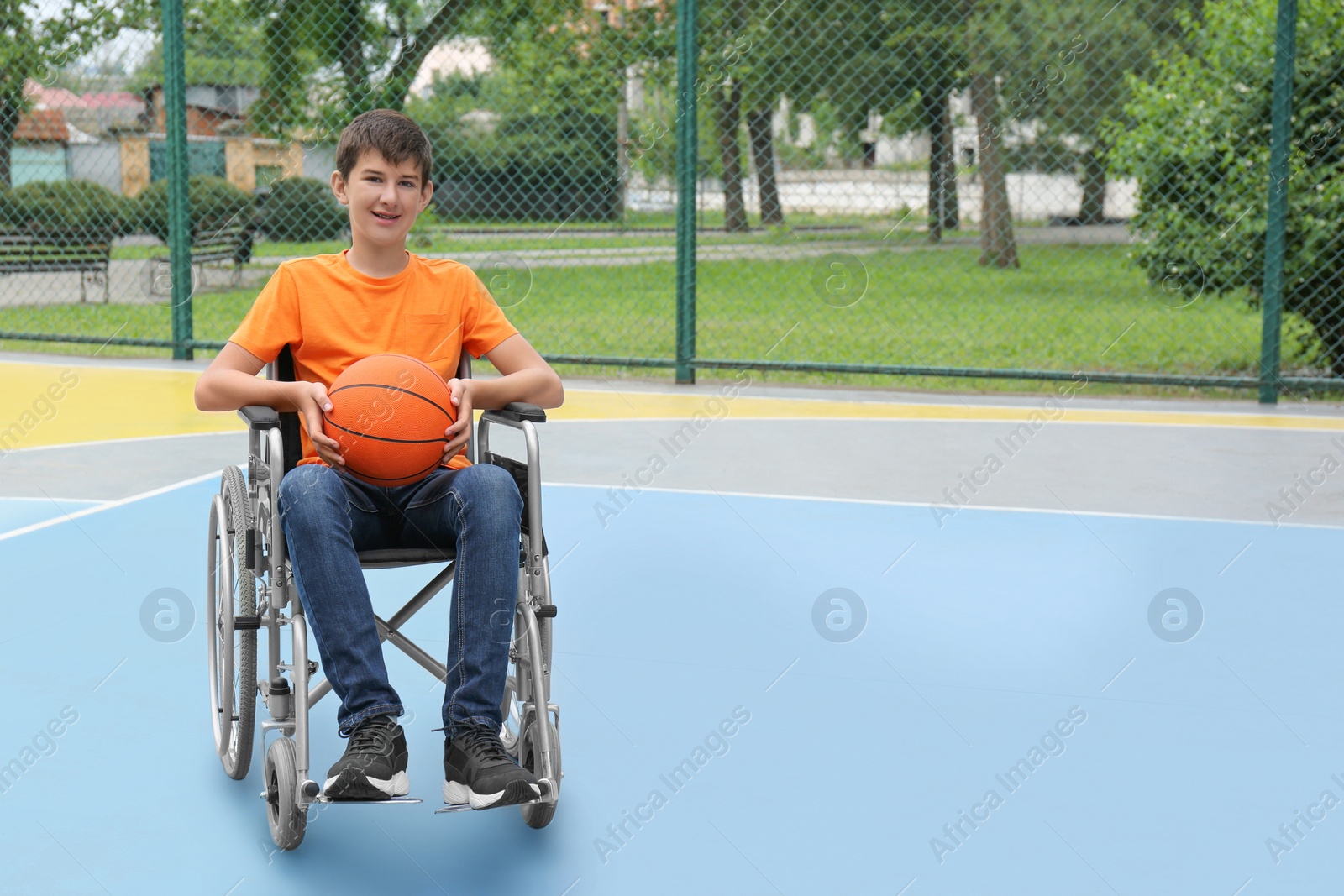 Photo of Disabled teenage boy in wheelchair with basketball ball at outdoor court