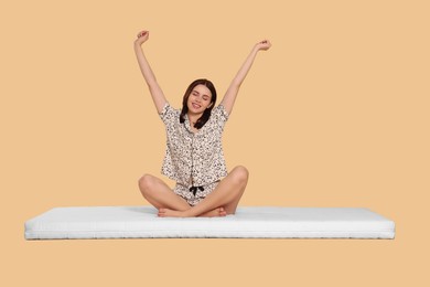 Young woman stretching on soft mattress against beige background