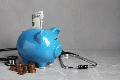 Photo of Piggy bank with money and stethoscope on light grey table, space for text. Medical insurance