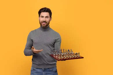 Photo of Smiling man showing chessboard with game pieces on yellow background. Space for text