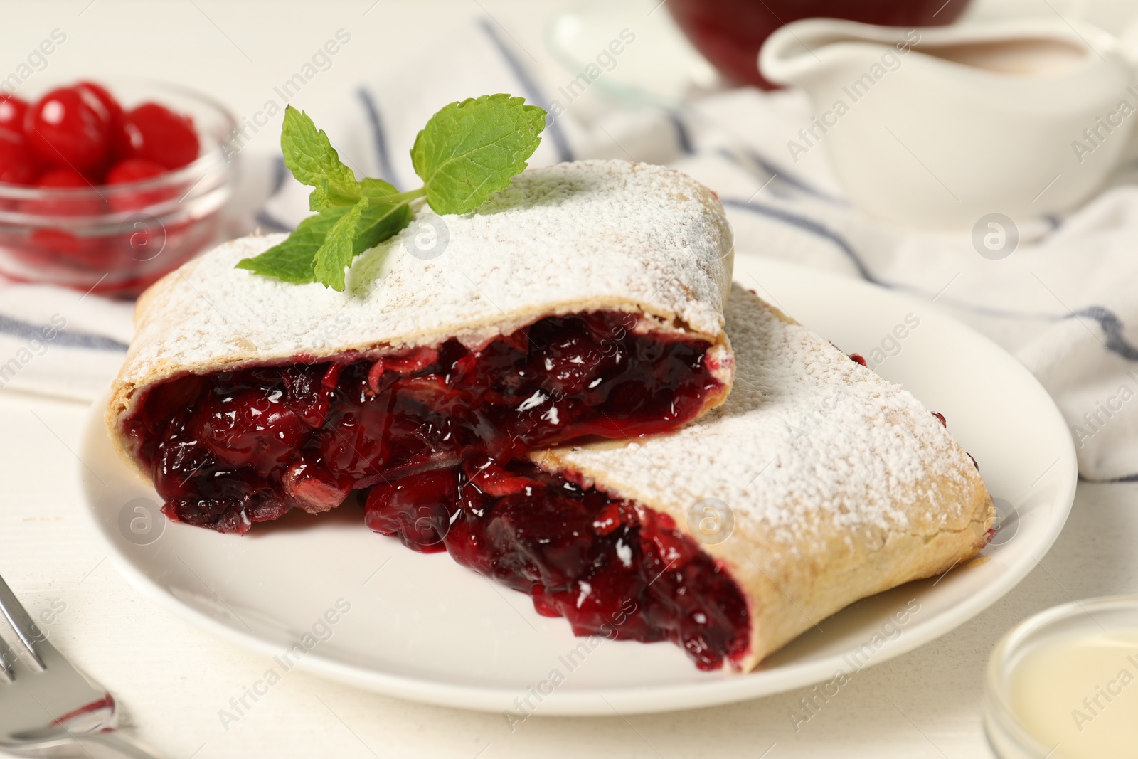 Photo of Delicious strudel with cherries, powdered sugar and mint on white table, closeup