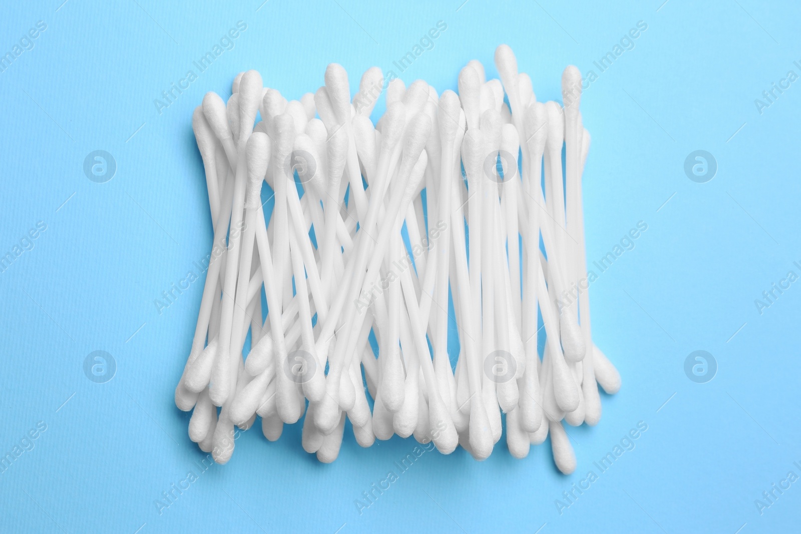 Photo of Heap of cotton buds on light blue background, top view