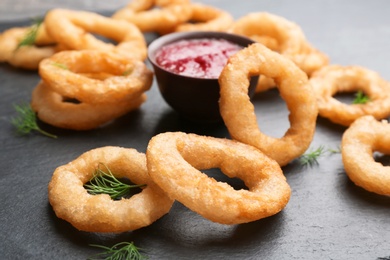 Photo of Fried onion rings and bowl of sauce on table, closeup