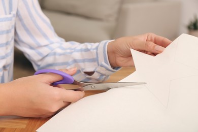 Photo of Woman cutting color paper with scissors at wooden table indoors, closeup