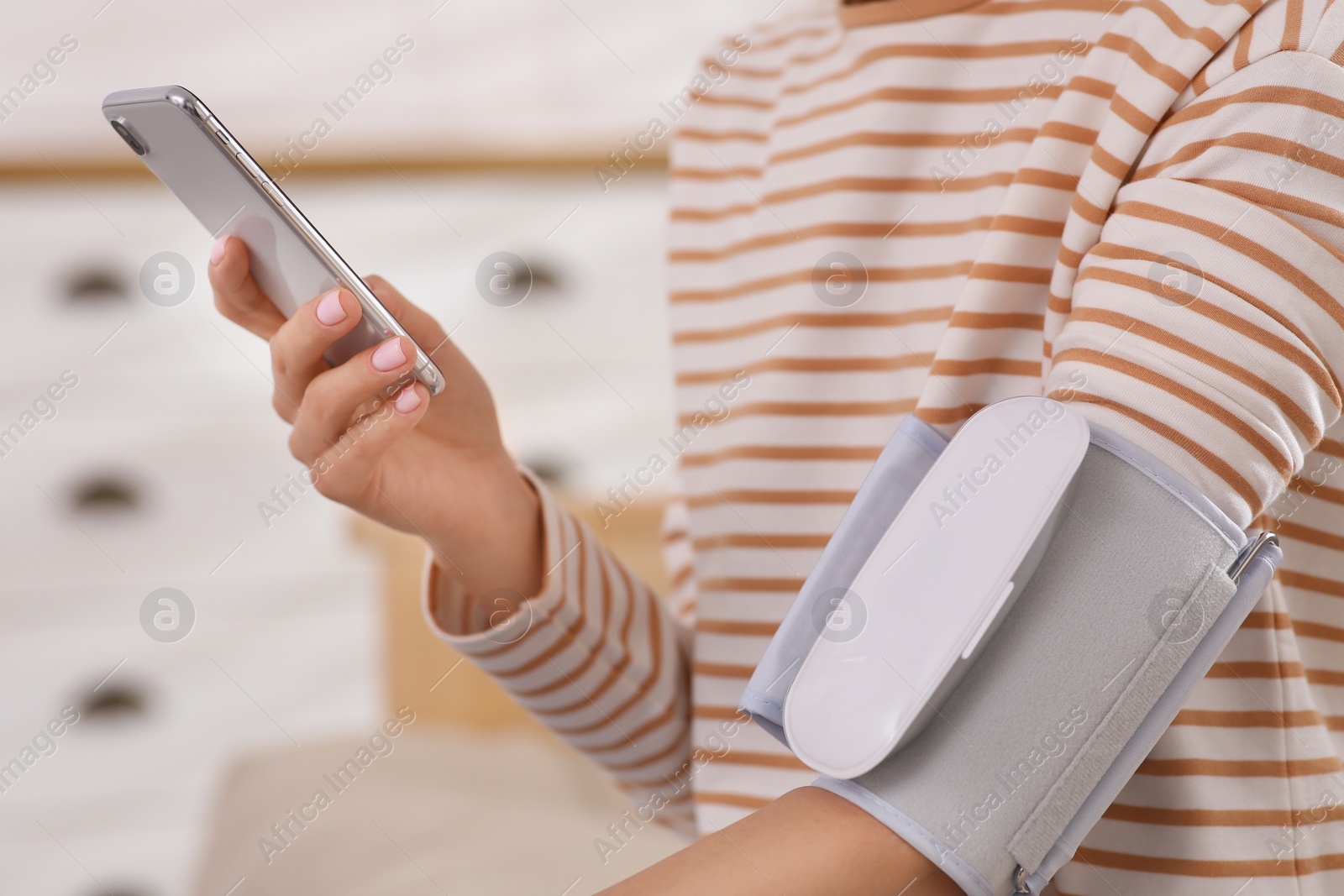 Photo of Woman checking blood pressure with modern monitor and smartphone indoors, closeup