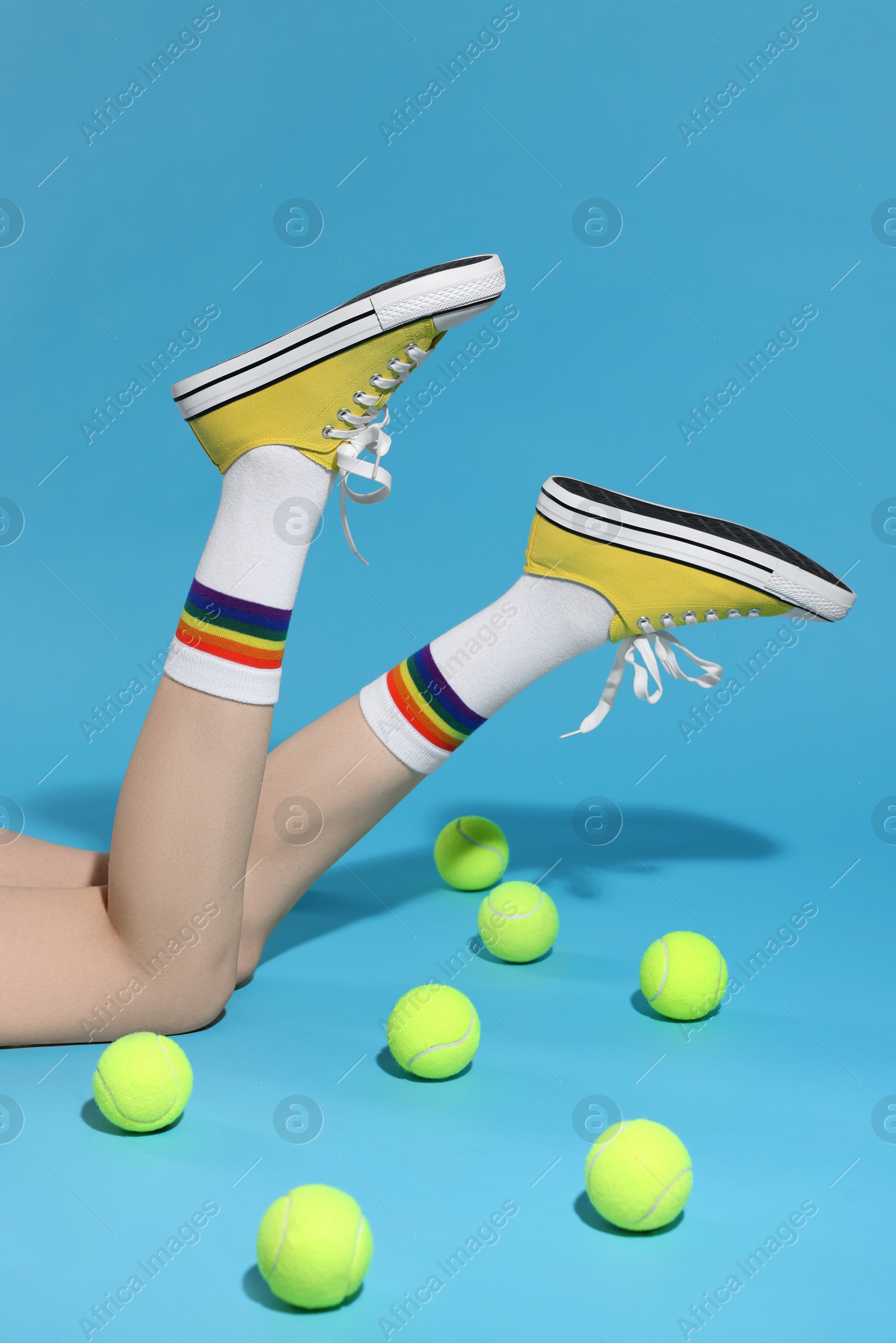 Photo of Woman posing in yellow classic old school sneakers and tennis balls on light blue background, closeup