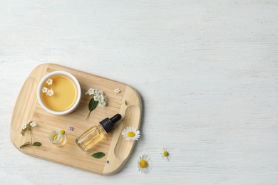 Photo of Flat lay composition with essential oil and flowers on white wooden table, space for text