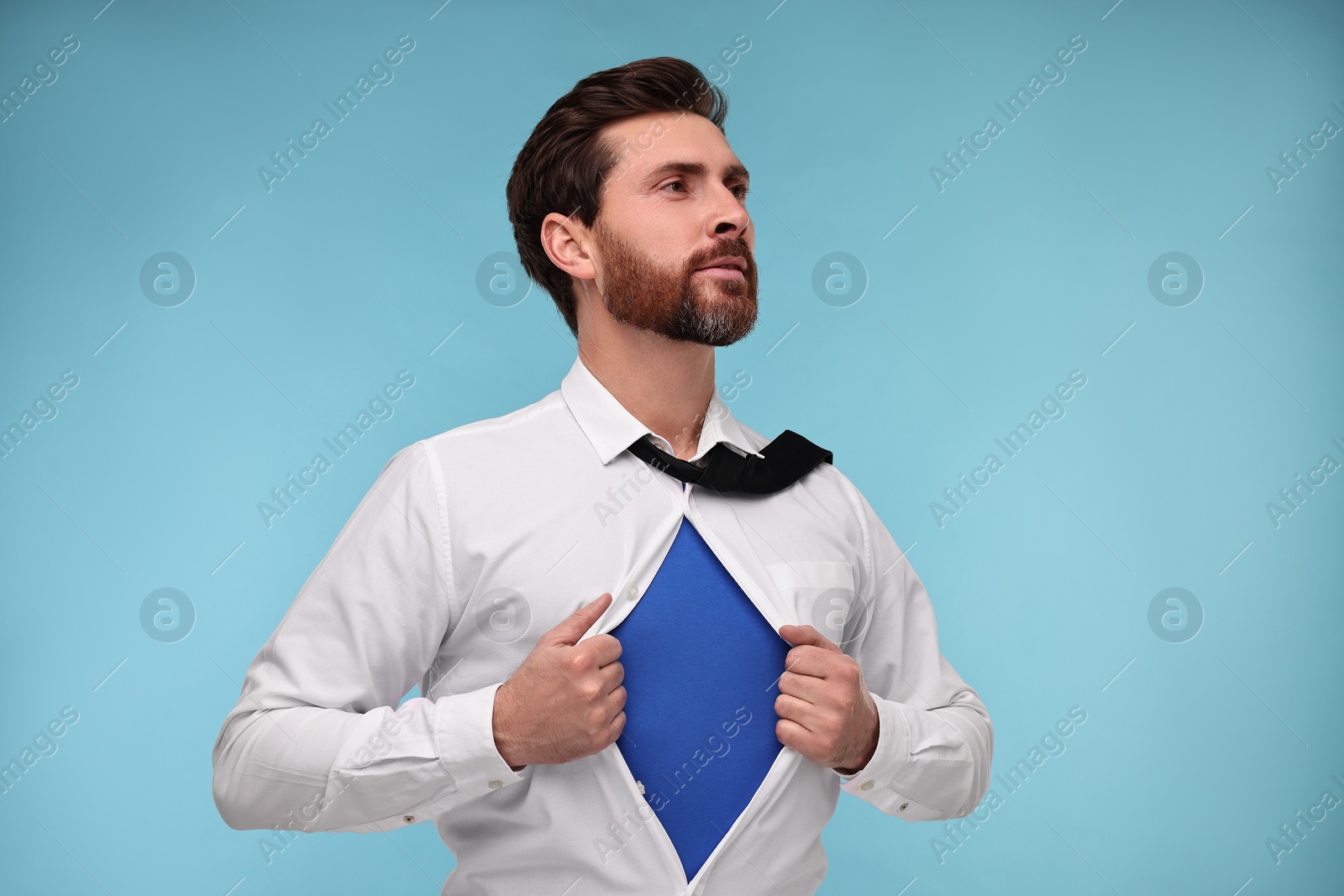 Photo of Confident businessman wearing superhero costume under suit on light blue background