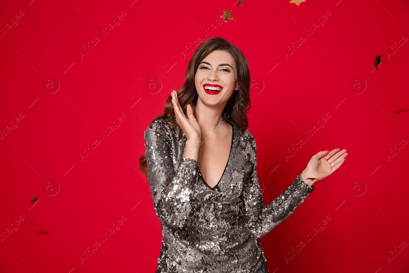 Photo of Happy woman in silver shiny dress and confetti on red background. Christmas party