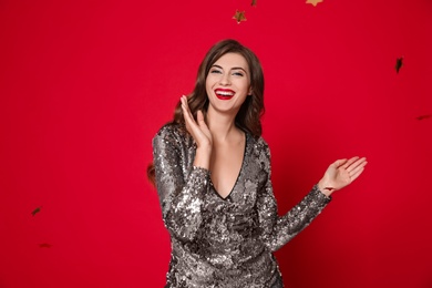 Happy woman in silver shiny dress and confetti on red background. Christmas party