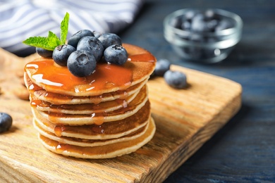 Wooden board with pancakes, syrup and blueberries on table, closeup