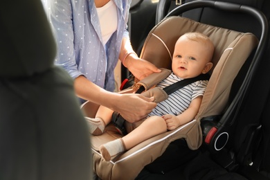 Mother fastening baby to child safety seat inside of car