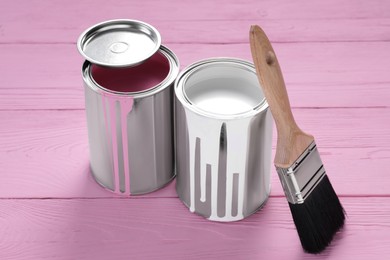 Cans of paints and brush on pink wooden table