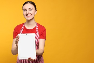 Photo of Beautiful young woman in clean striped apron with tablet on orange background. Space for text