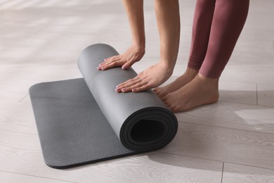 Photo of Woman unrolling yoga mat at home, closeup