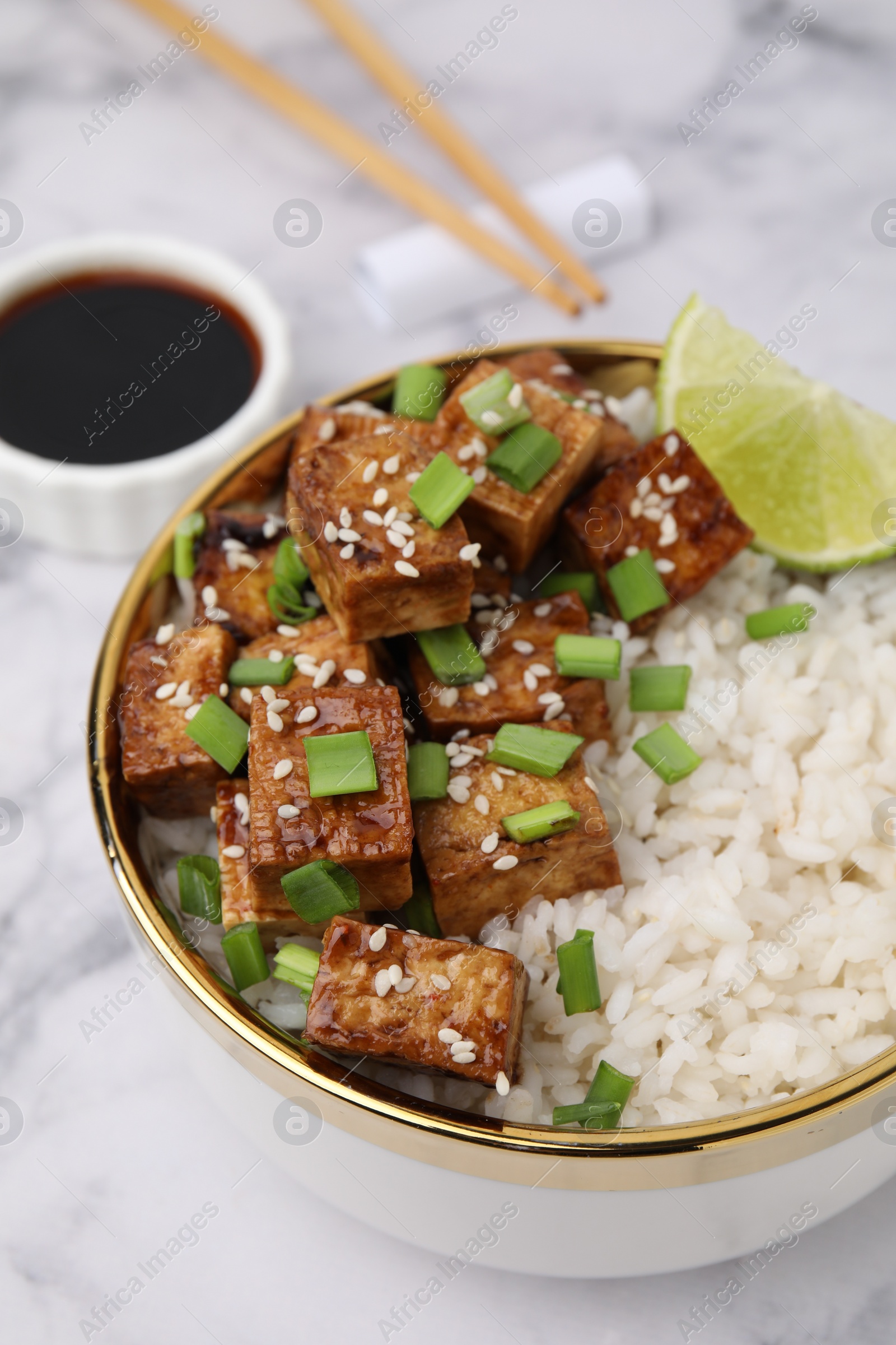 Photo of Bowl of rice with fried tofu and green onions on white marble table, closeup