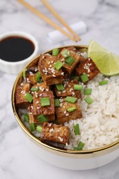 Bowl of rice with fried tofu and green onions on white marble table, closeup