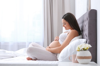 Photo of Young beautiful pregnant woman sitting on bed and touching her belly at home