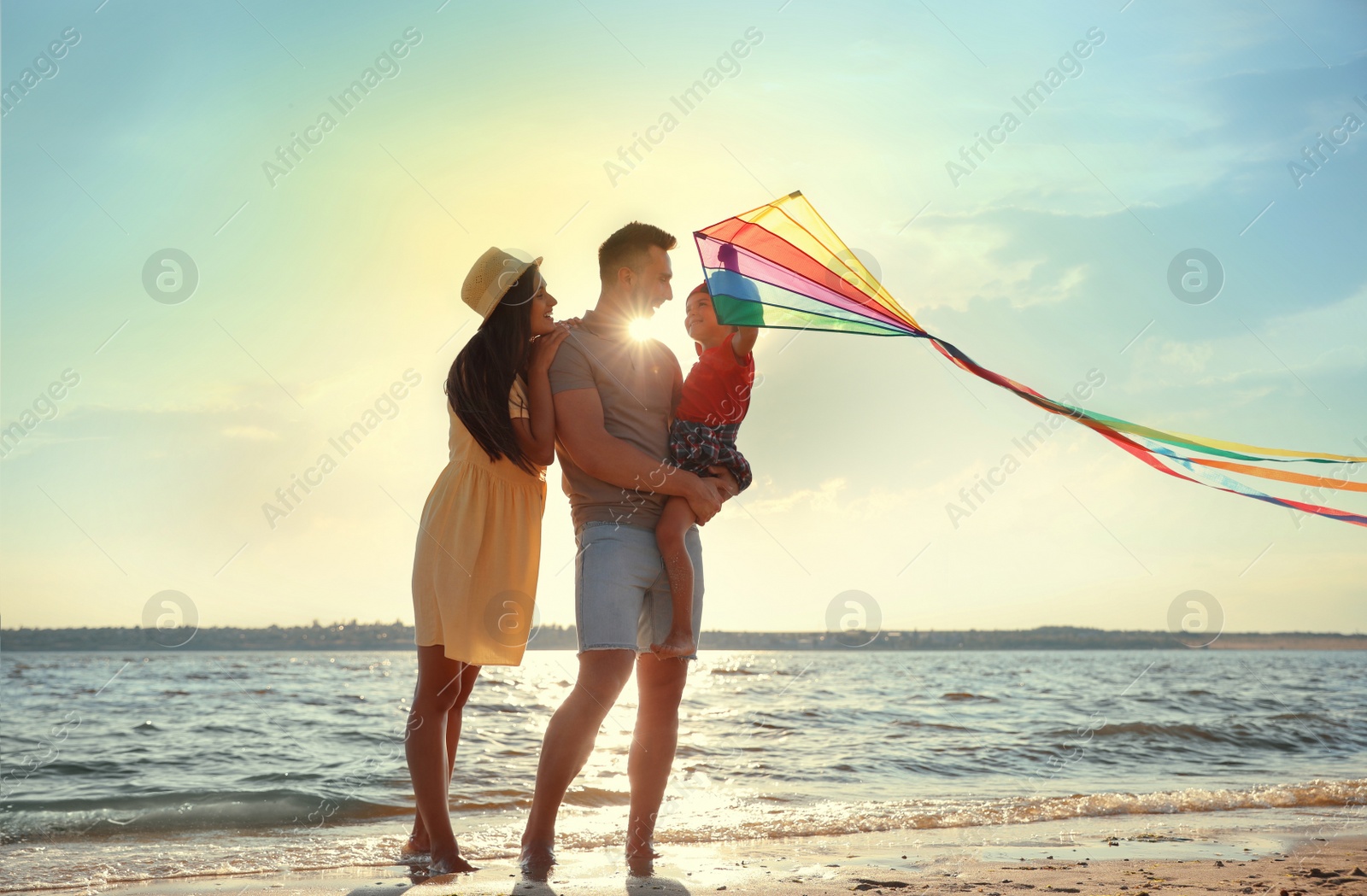Photo of Happy parents and their child playing with kite on beach near sea. Spending time in nature