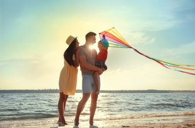 Photo of Happy parents and their child playing with kite on beach near sea. Spending time in nature