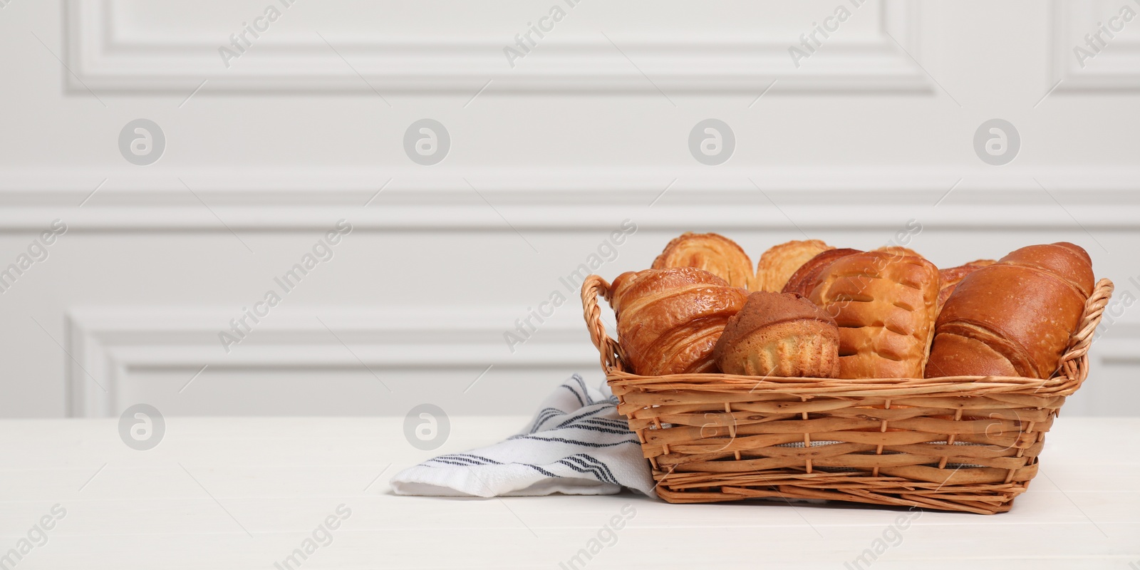 Photo of Wicker basket with different tasty freshly baked pastries on white wooden table, space for text