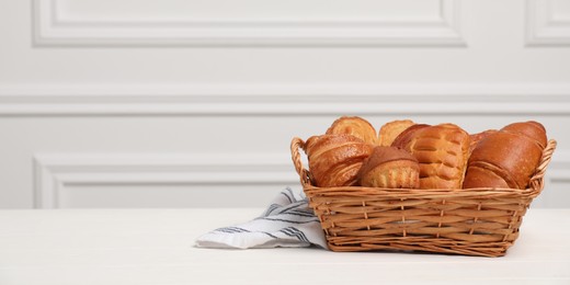 Wicker basket with different tasty freshly baked pastries on white wooden table, space for text