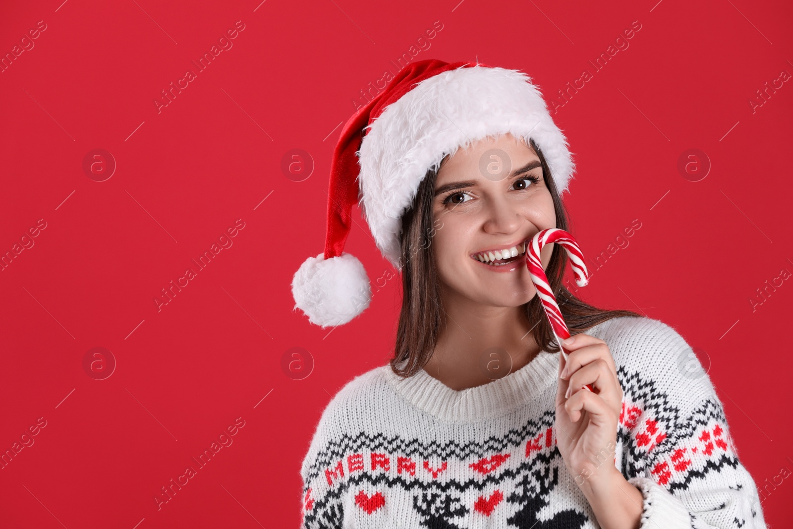 Photo of Pretty woman in Santa hat and Christmas sweater holding candy cane on red background