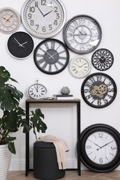 Photo of Console table, beautiful houseplant and collection of different clocks on white wall in room
