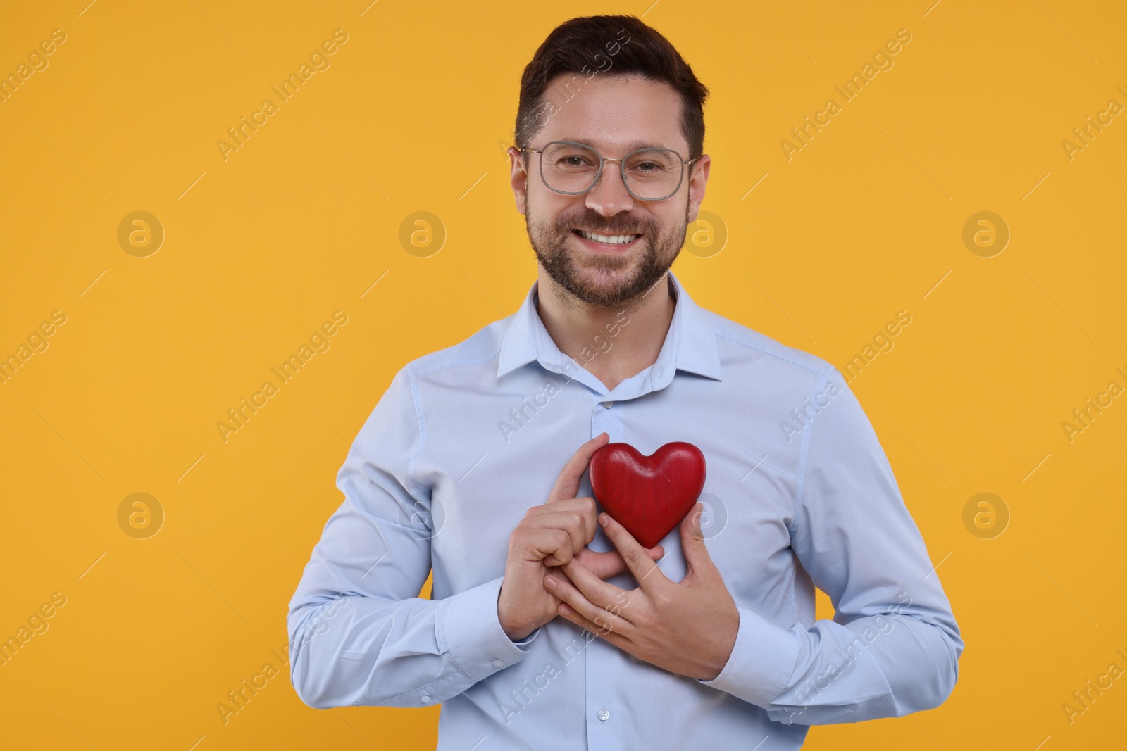Photo of Happy man holding red heart on yellow background